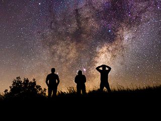 Three silhouetted figures look at a star-filled sky. Three silhouetted figures look at a star-filled sky.
