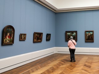 A person stands alone in a museum gallery, looking at paintings. A person stands alone in a museum gallery, looking at paintings.