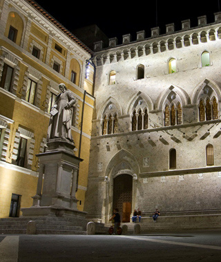 The Piazza Salimbeni in Sienna, Italy at night, showing the facade of the Banca Monte dei Paschi di Siena,Tito Sarrocchi’s statue of Sallustio Bandini, and several people, including a child on a bicycle. The Piazza Salimbeni in Sienna, Italy at night, showing the facade of the Banca Monte dei Paschi di Siena,Tito Sarrocchi’s statue of Sallustio Bandini, and several people, including a child on a bicycle.