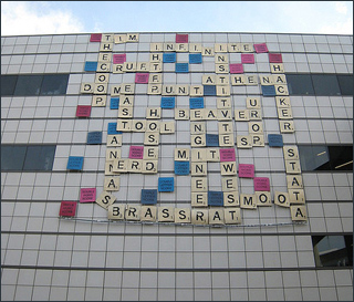 On the side of a building hang multi-colored squares, each with a letter or phrase on them, simulating a Scrabble game. On the side of a building hang multi-colored squares, each with a letter or phrase on them, simulating a Scrabble game.
