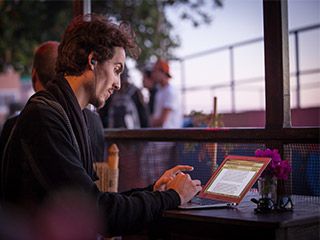 A curly-haired young man, with an earpiece hanging from his ear, types on a laptop. A curly-haired young man, with an earpiece hanging from his ear, types on a laptop.