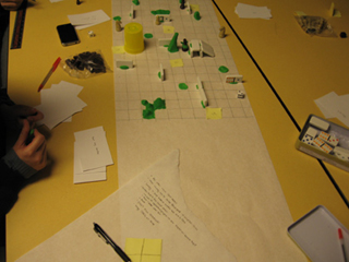 A paper grid with various obstacles of Play-Doh and dominos functions as a board for a game with tokens and dice. A paper grid with various obstacles of Play-Doh and dominos functions as a board for a game with tokens and dice.