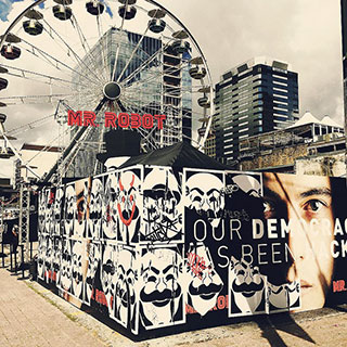 A photo of a ferris wheel with the words, "Mr. Robot" on it. In the foreground are two walls plastered with posters from the TV series. A photo of a ferris wheel with the words, "Mr. Robot" on it. In the foreground are two walls plastered with posters from the TV series.