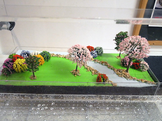 Diorama of a grassy park and trees with water in front. Diorama of a grassy park and trees with water in front.