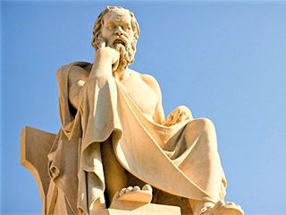 A marble statue of a seated, toga-wearing man with a furrowed brow and one hand resting on his chin. A marble statue of a seated, toga-wearing man with a furrowed brow and one hand resting on his chin.