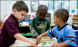 At a table, three small boys play with puzzles. At a table, three small boys play with puzzles.