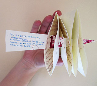 Photo of a hand holding a folded piece of paper with another strip of paper piercing through it to form a locked letter. The paper lock reads: This is a paper lock, now a papered seal with signet impression. The sealing wax acts as an adhesive. Photo of a hand holding a folded piece of paper with another strip of paper piercing through it to form a locked letter. The paper lock reads: This is a paper lock, now a papered seal with signet impression. The sealing wax acts as an adhesive.