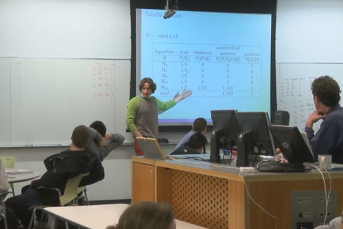<p>Students were expected to complete assigned readings and reading questions before class and we structured our teaching to build on this preparation. Lectures were brief summaries, kept short to allow ample time for active learning. We aimed to have students working on a problem within the first 15 minutes of class.</p> <p>For each class session, we created a slide deck that contained lecture content as well as problems for the students to work on. After class, we added full solutions to the slide deck and posted everything online for student use.</p> An instructor points at a projector screen showing a slide and addresses students, who are sitting at round tables.