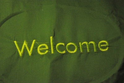 Photo of fabric embroidered with the word ‘Welcome’ in a Helvetica-style font.