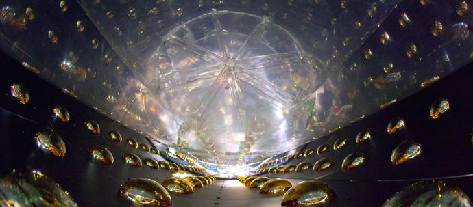 An array of bright yellow hemispheres line the outside of a irregularly shaped dark metal chamber, with a lit transparent element at the bottom. An array of bright yellow hemispheres line the outside of a irregularly shaped dark metal chamber, with a lit transparent element at the bottom.