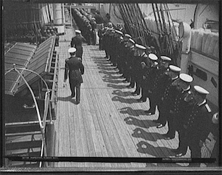 A black and white photo of two officers inspecting sailors on deck. A black and white photo of two officers inspecting sailors on deck.