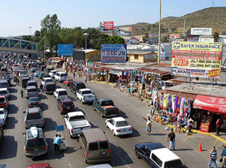 Cars wait in line on a road lined with shops at the US/Mexican border. Cars wait in line on a road lined with shops at the US/Mexican border.