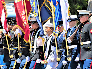 A group of six men and two women, all-uniformed, with some carrying colorful flags, marches in formation. A group of six men and two women, all-uniformed, with some carrying colorful flags, marches in formation.