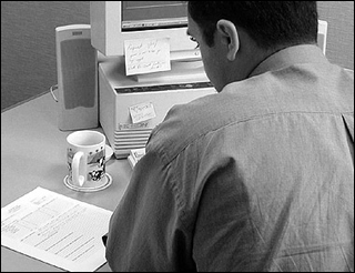 Black-and-white photograph of a businessman writing a memo in front of a computer. Black-and-white photograph of a businessman writing a memo in front of a computer.