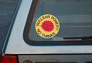 A yellow and red round sticker about anti-nuclear power is on the back window of a car. A yellow and red round sticker about anti-nuclear power is on the back window of a car.
