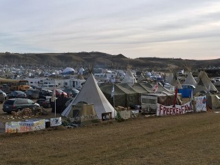 A cluster of tents, tipis, and parked vehicles in an open, treeless landscape. A cluster of tents, tipis, and parked vehicles in an open, treeless landscape.