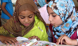 Two girls in headscarves read together from a book. Two girls in headscarves read together from a book.