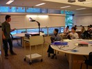 Students sit around tables listening to a teacher talk about overhead filters.