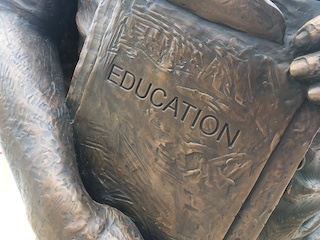 Photo of a metal statue holding a book that says "Education." Photo of a metal statue holding a book that says "Education."